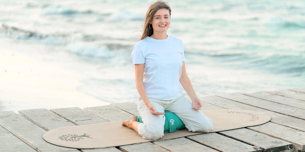 Jasmin Patricia Kremer, Gründerin von FLOWALOHA, sitzt am Meer auf der ovalen Yogamatte Kork und auf dem meeresgrünen Meditationskissen aus Baumwolle. Sie dreht gerade ihren Online Yogakurs.