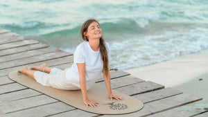 Auf dem Bild siehst Du die Gründerin von FLOWALOHA Jasmin Patricia Kremer auf der ovalen Kork Yogamatte Kalea in der Yogaübung die große Kobra auf einem Steg am Strand von Mallorca. Die Yogamatte oval ist sehr rutschfest, gelenkschonend und nachhaltig. Sie ist der Testsieger bei den Kunden. Bekannt wurde die Marke durch den Sparkassen Gründerpreis BW 2024, Yogaworld und YogaAktuell.